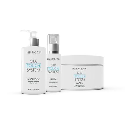 The Silk Touch System Duo Bundle from Hair Bar NYC is displayed, featuring a pump shampoo bottle, a pump serum bottle, and a mask jar—all with minimalist white labels accented by blue and black text.